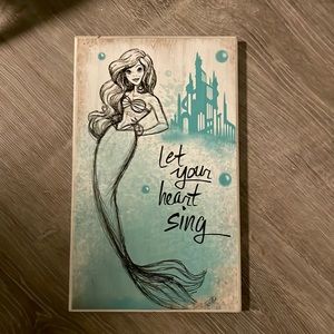 A hanging picture of ariel with blue background and her castle in the back